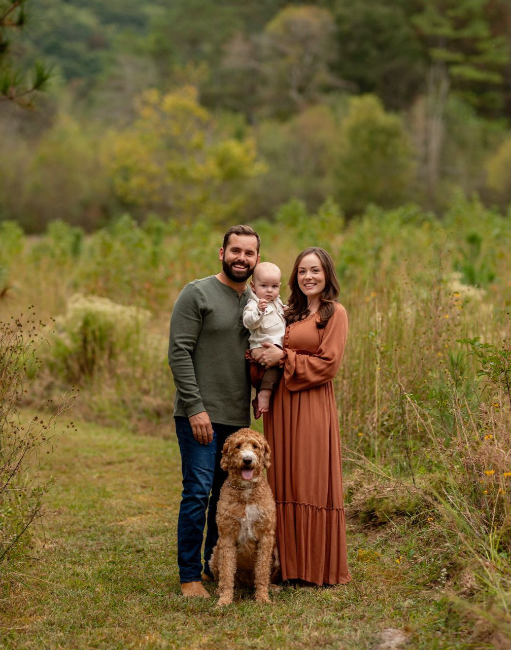 A family is posing for a picture with a baby and a dog.