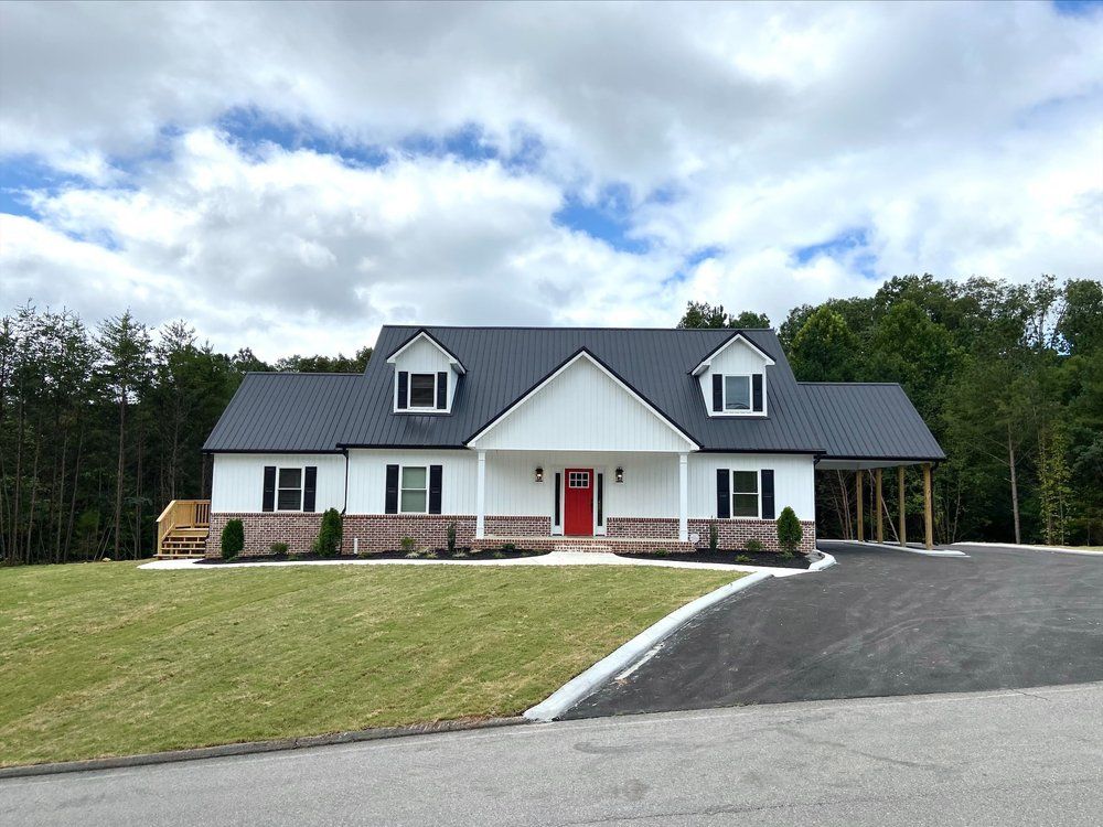 A white house with a black roof and a red door is sitting on top of a lush green hillside.