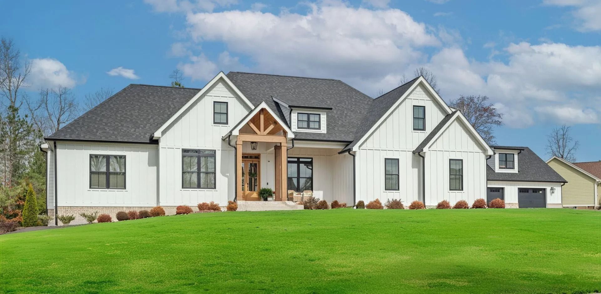 White modern farmhouse with dark roof and large green lawn under a blue sky