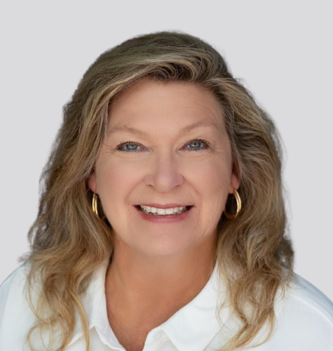 A woman with curly hair is wearing a blue jacket and smiling.