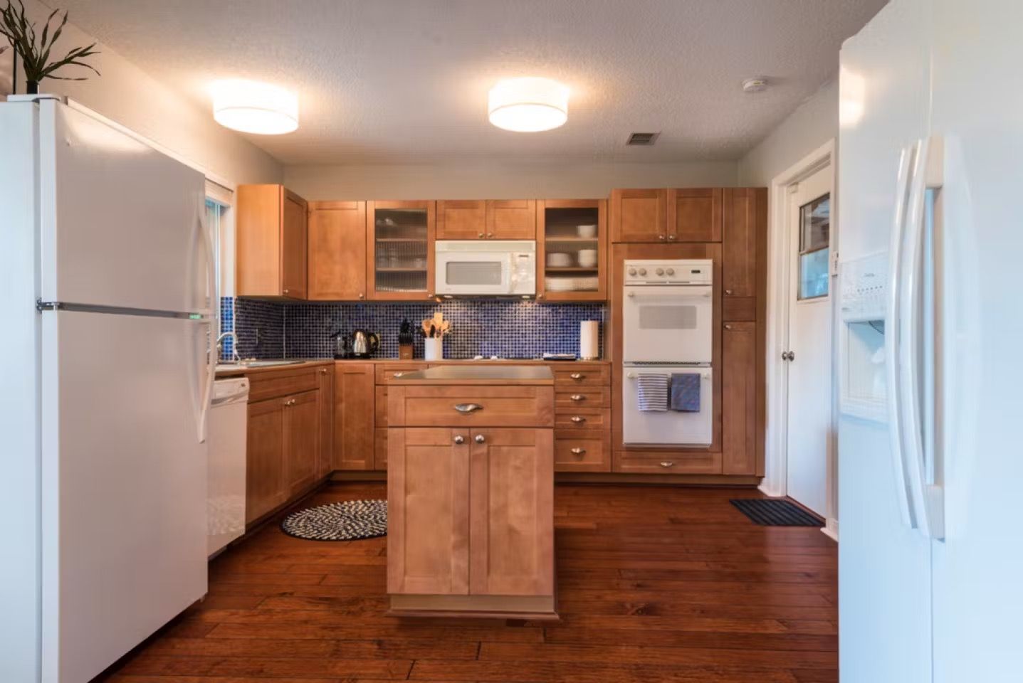 Bright kitchen with white appliances, wood cabinets, tiled backsplash, and a central island.