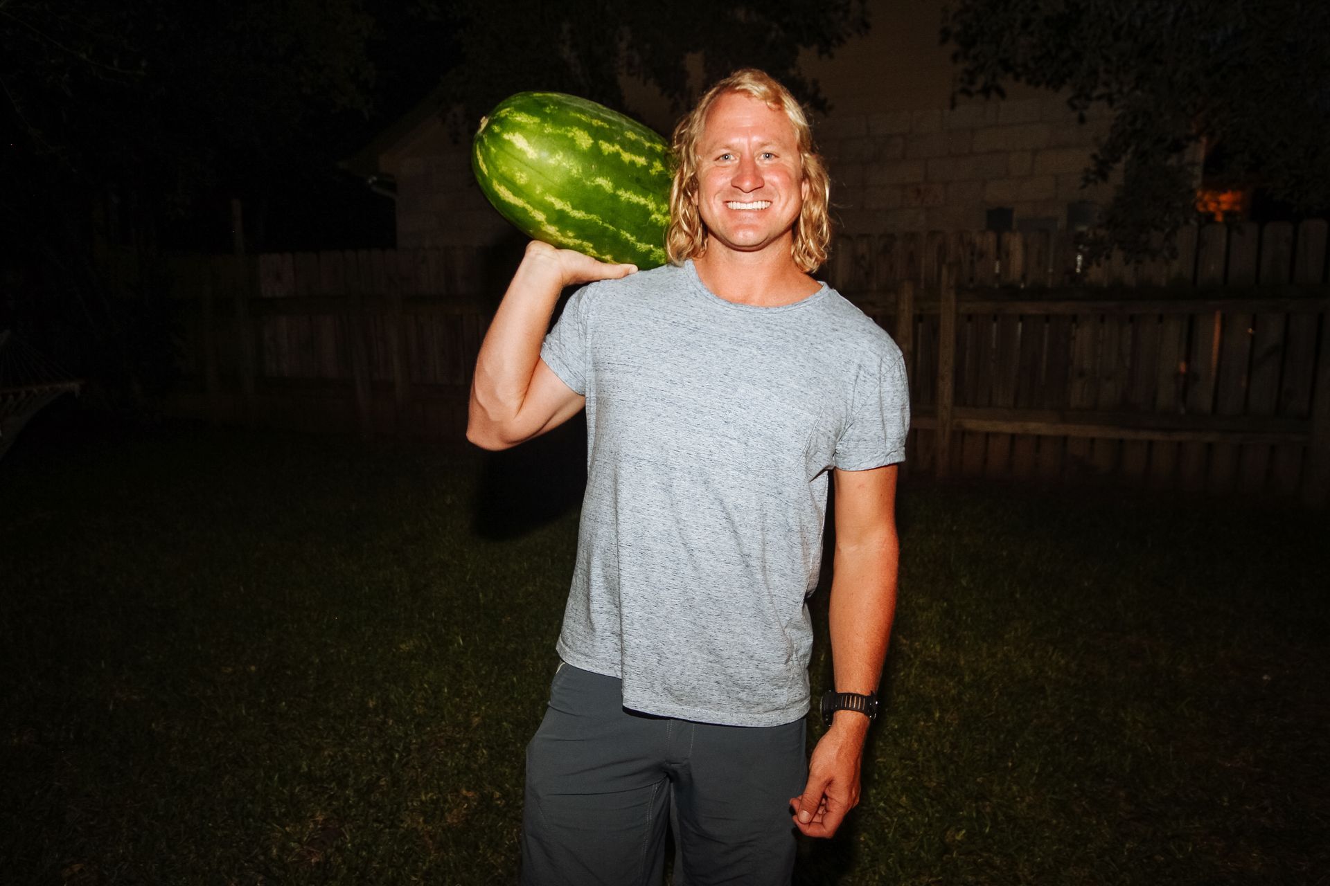 Person holding a large green melon on their shoulder outdoors at night