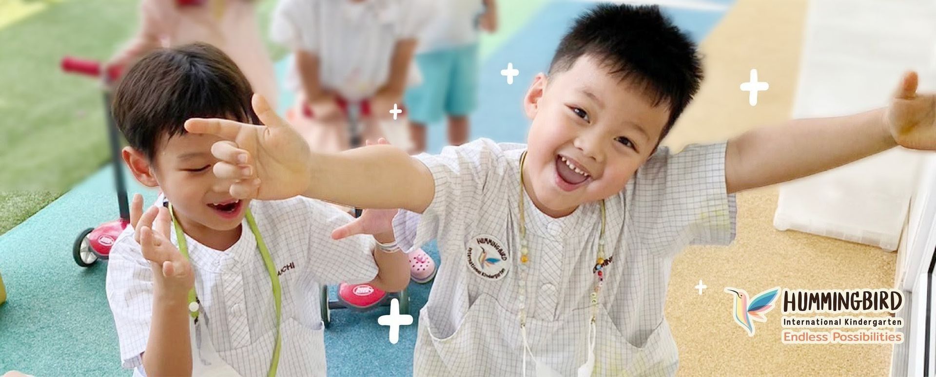 Two young children with open arms, smiling, in a playful outdoor setting.