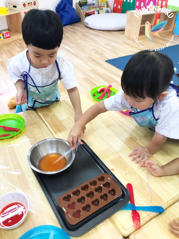 Two children are playing with a chocolate mould with hearts on it