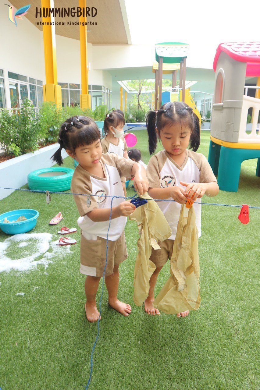 Two little girls are playing with a piece of paper on the grass.