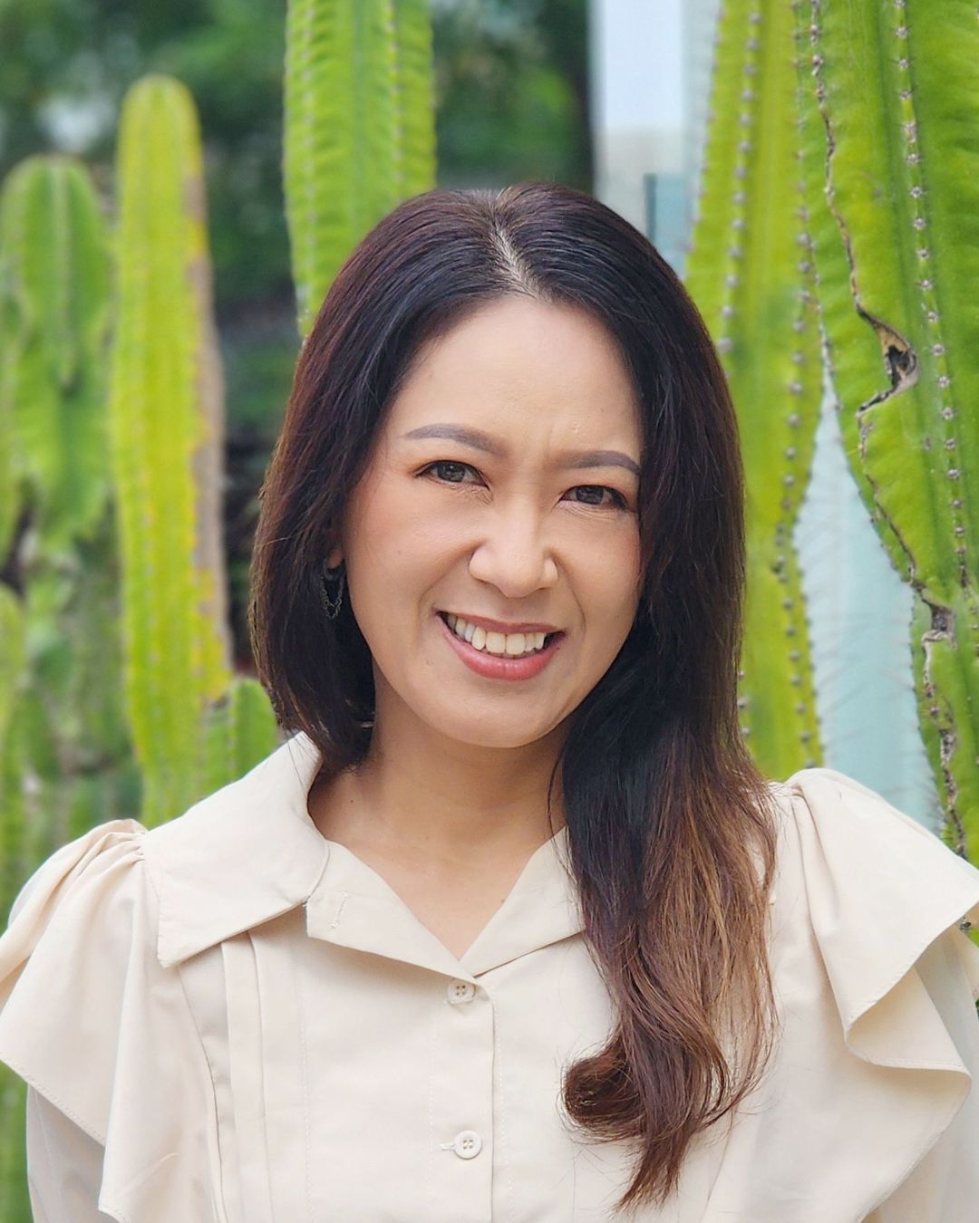 A woman in a white shirt and black vest is smiling with her arms crossed.