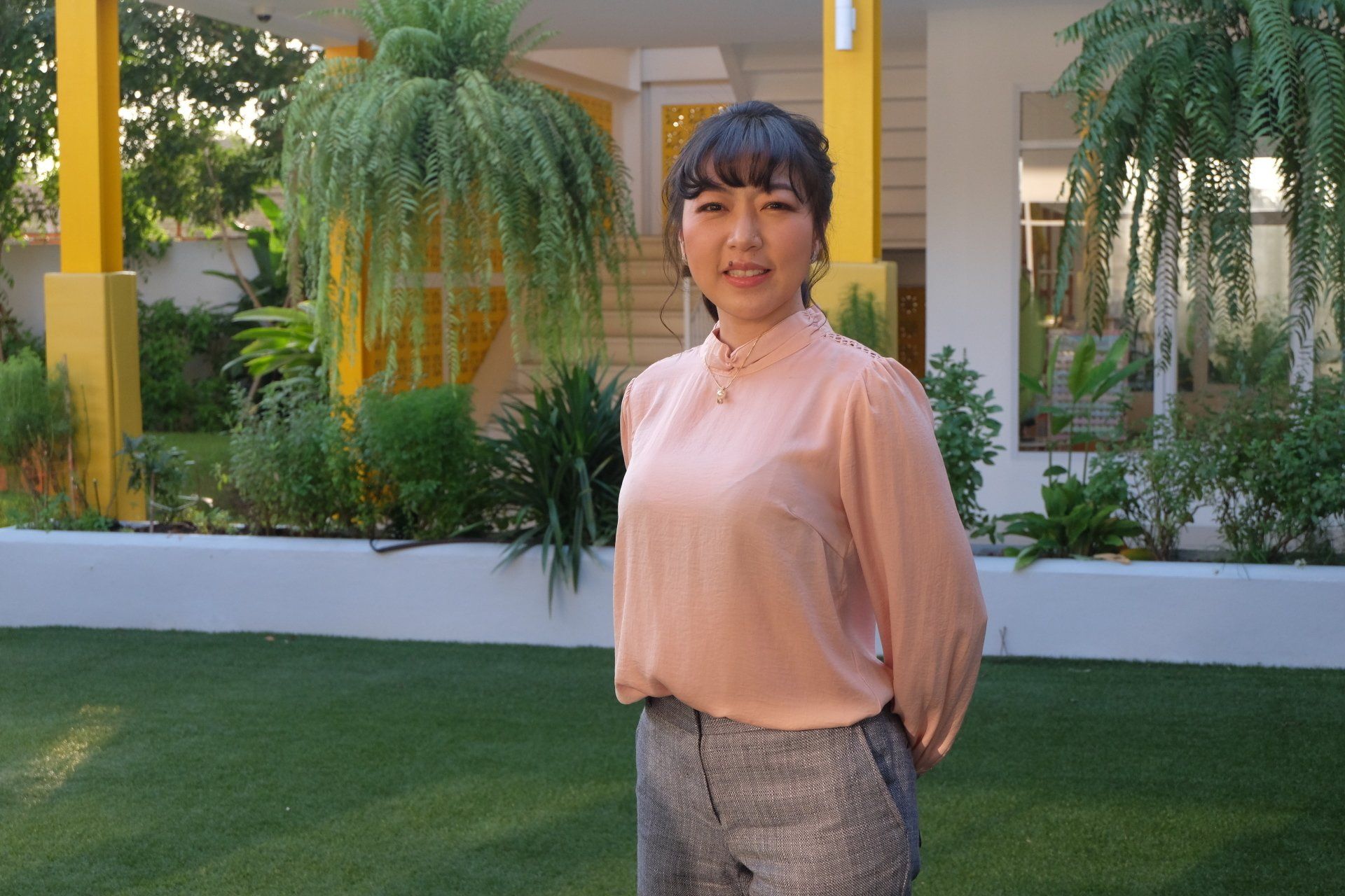 A woman in a pink shirt is standing in front of a house.