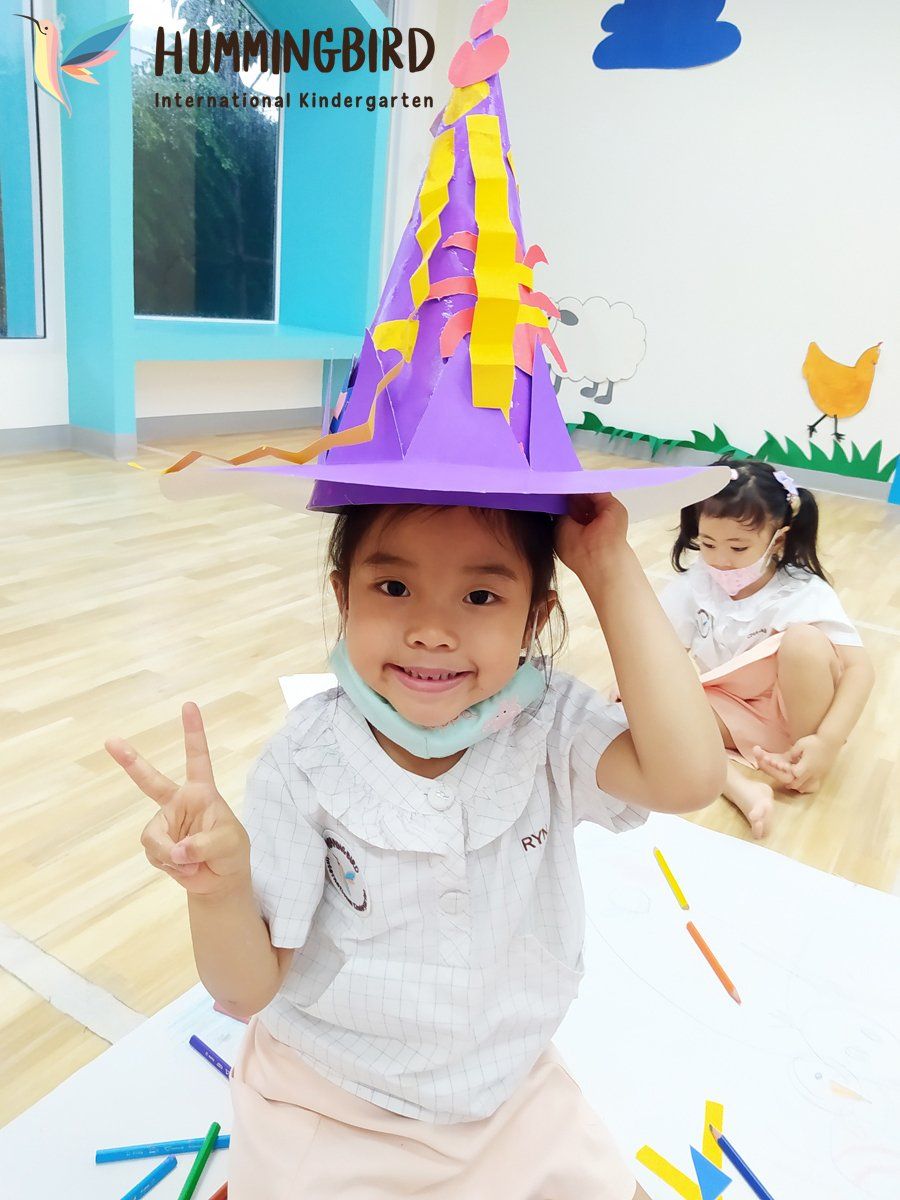 A little girl wearing a purple hat is giving a peace sign.