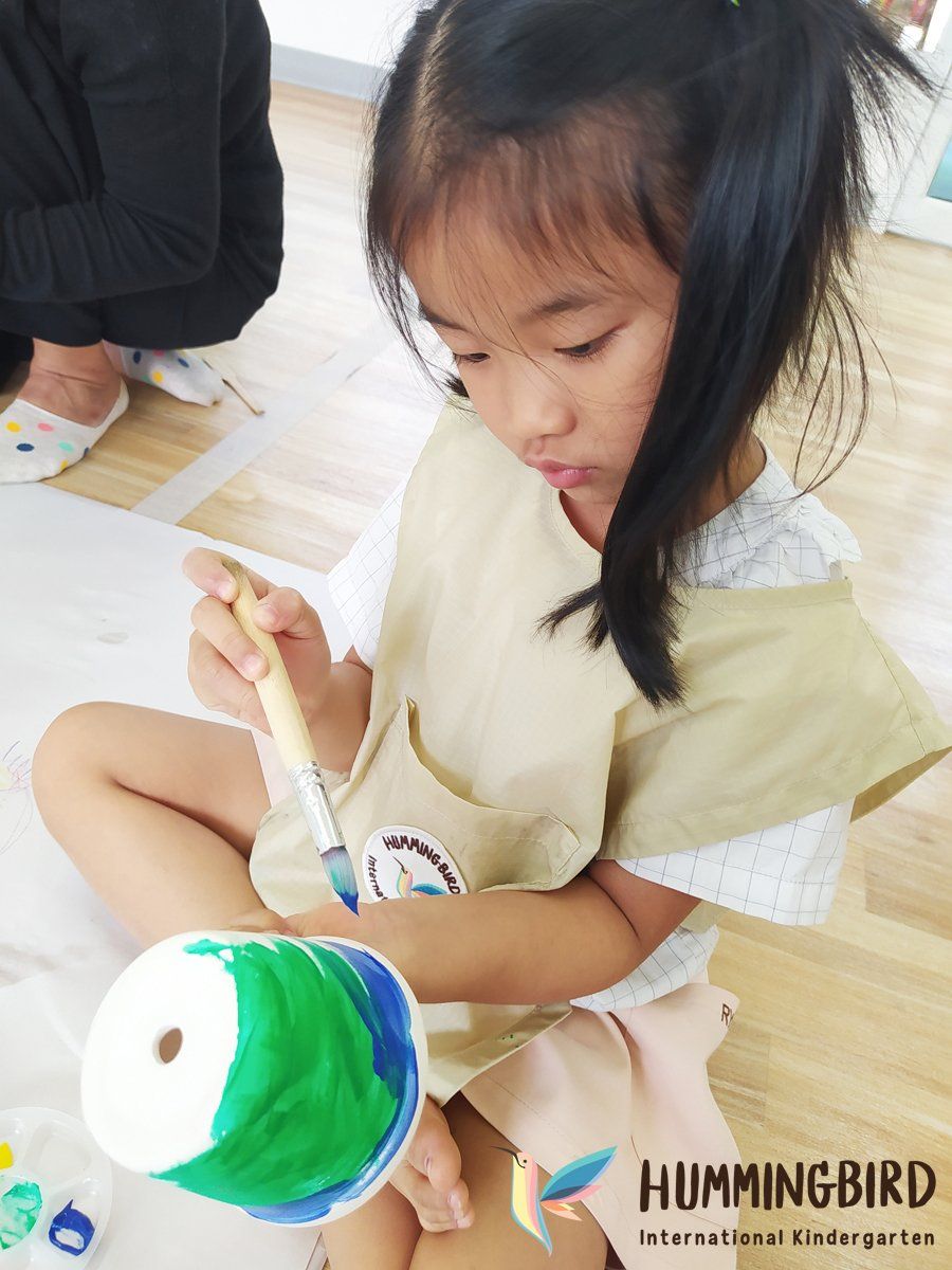A little girl is sitting on the floor painting a cup with a brush.