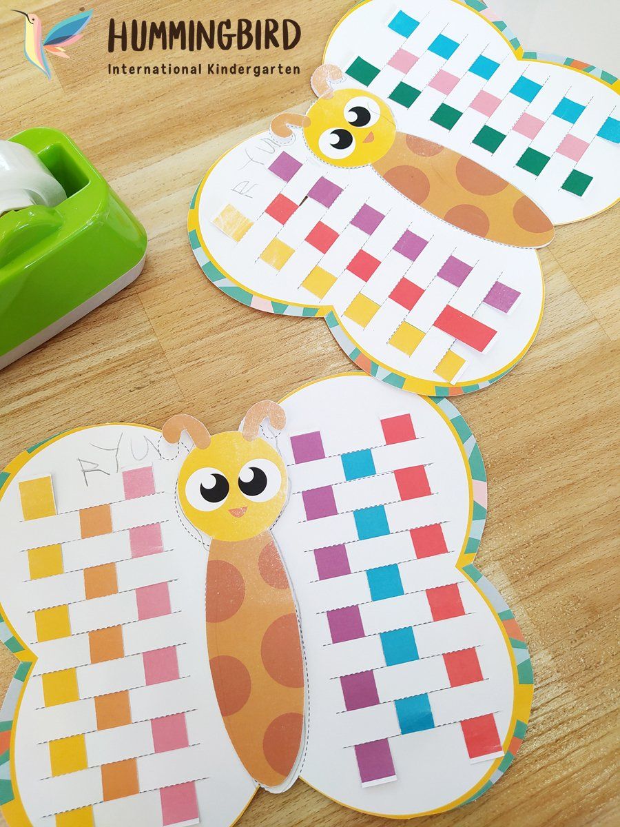 Two butterfly crafts are sitting on a wooden table next to a tape dispenser.