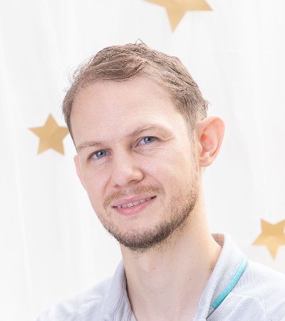 A man with a beard is smiling for the camera in front of a white curtain with stars.