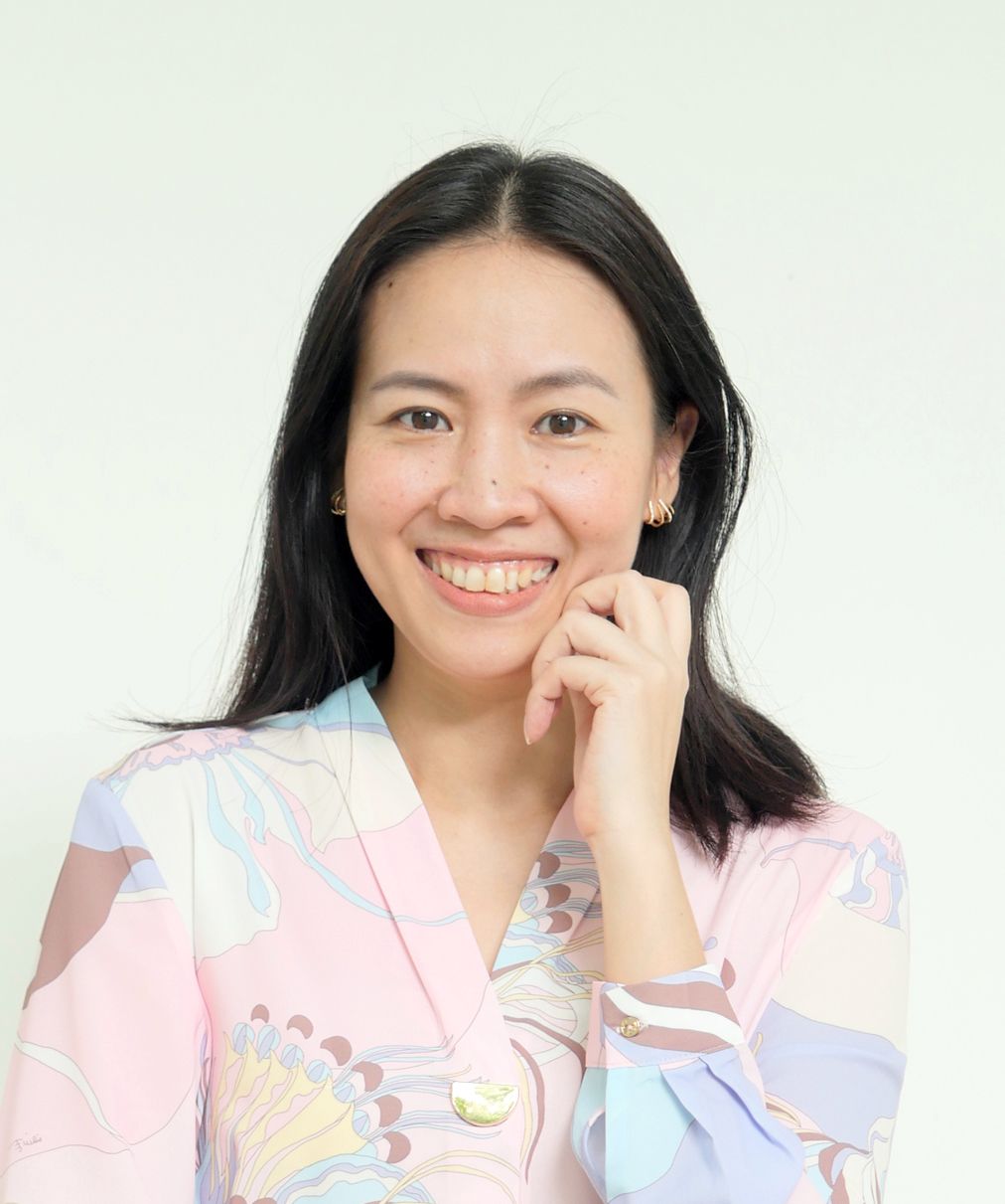 A woman in a pink pleated shirt is smiling for the camera