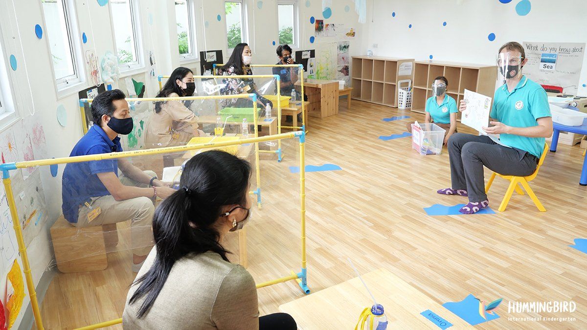 A group of people wearing masks are sitting around a table in a room.