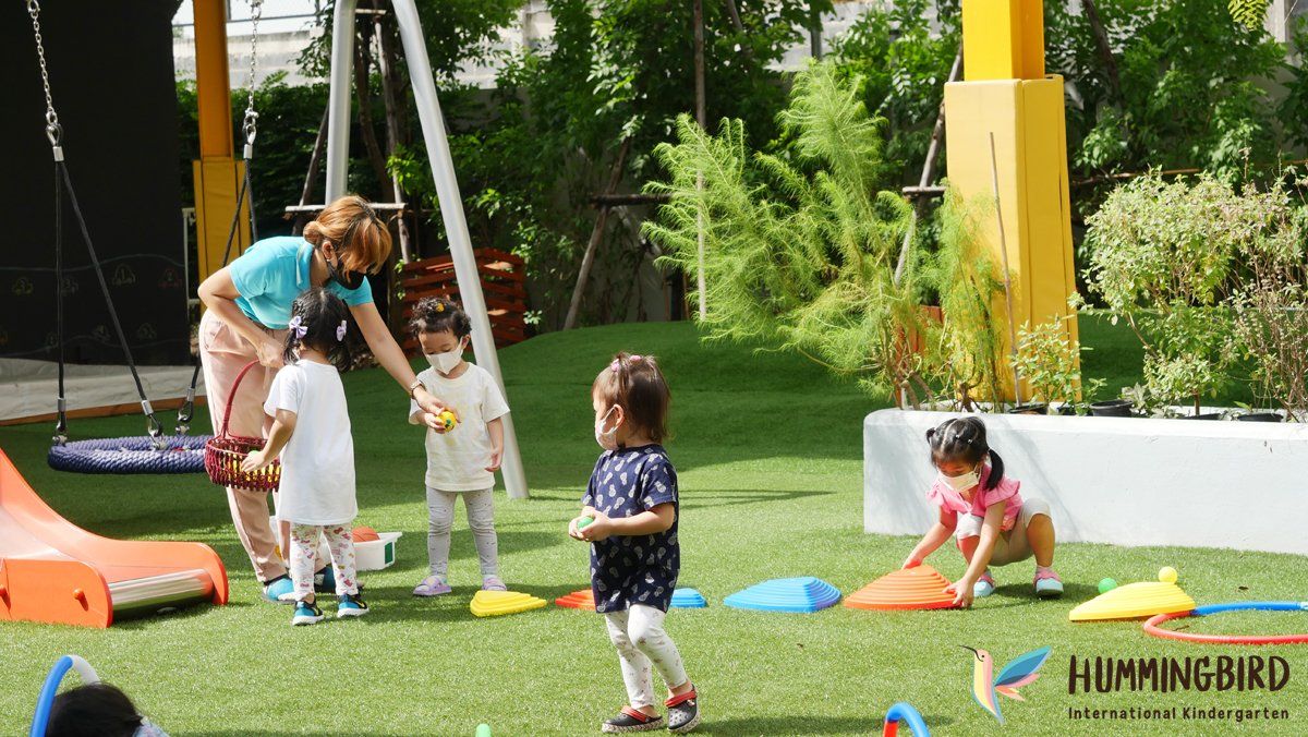 A group of children are playing in a park with a woman.
