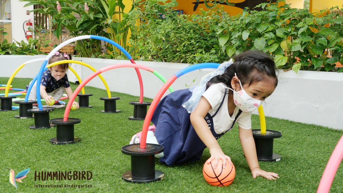 A little girl wearing a mask is playing with a basketball on the grass.