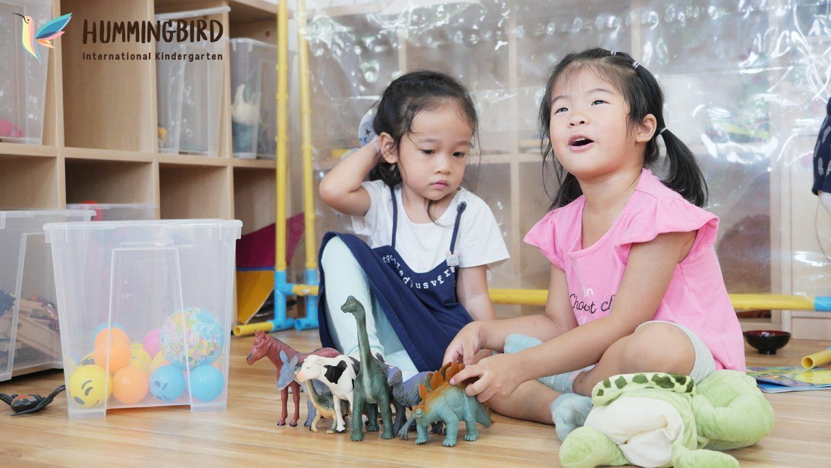Two little girls are sitting on the floor playing with toy dinosaurs.