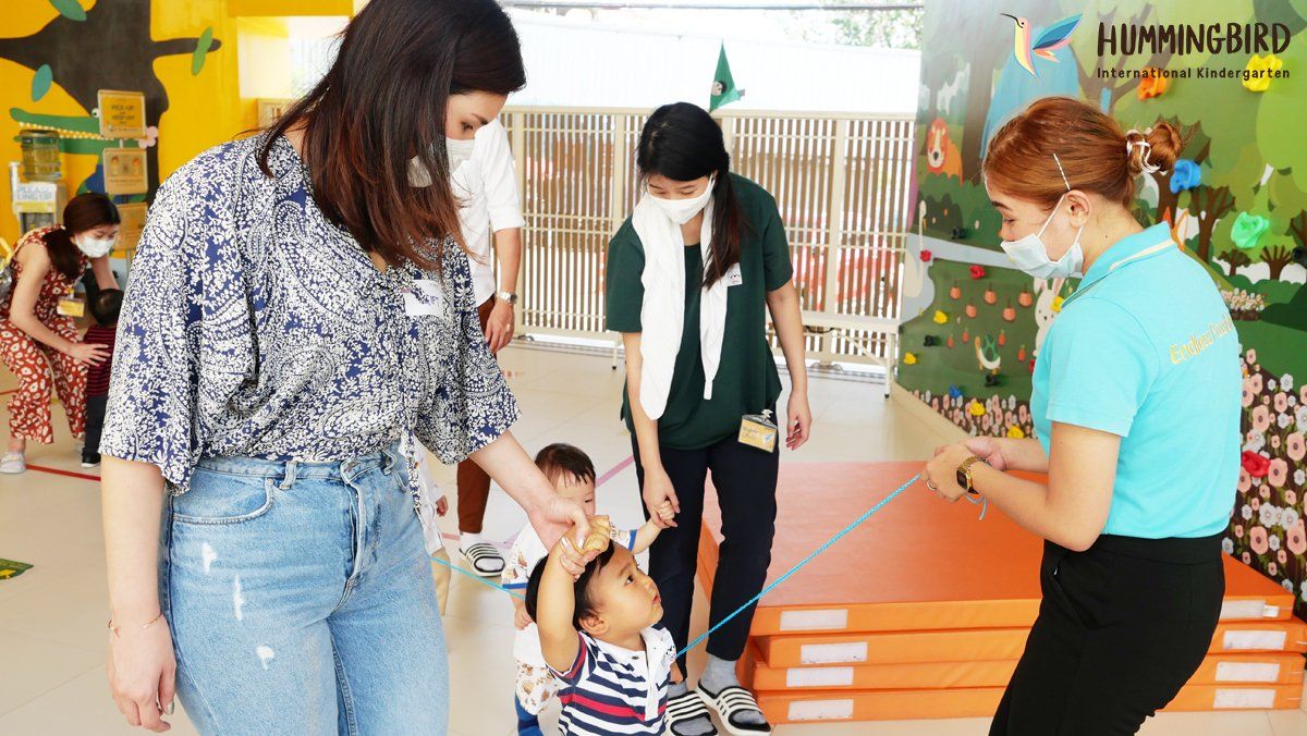 A woman is holding a child 's hand in a room with other people.