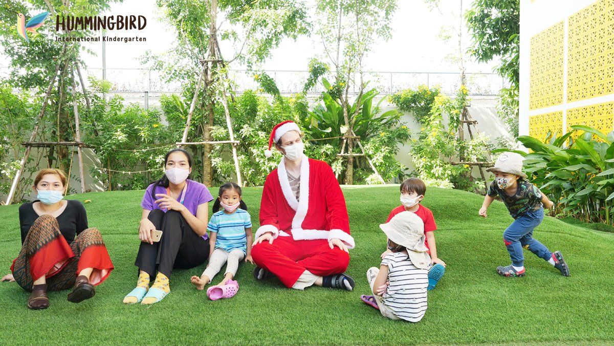 A group of people wearing face masks are sitting on the grass with a man dressed as santa claus.