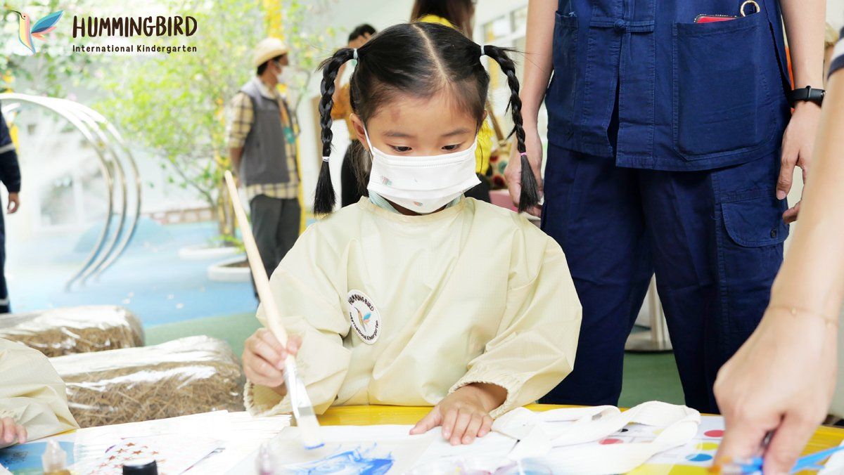 A little girl wearing a mask is painting with a brush.