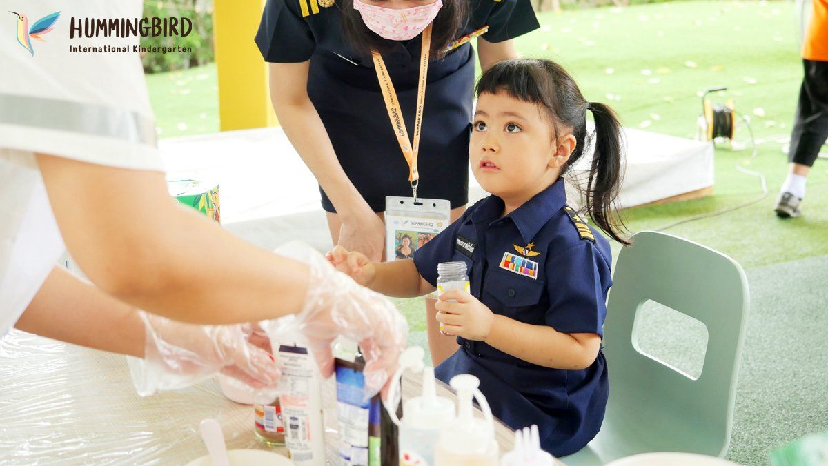 A little girl is sitting at a table holding a cup of milk.