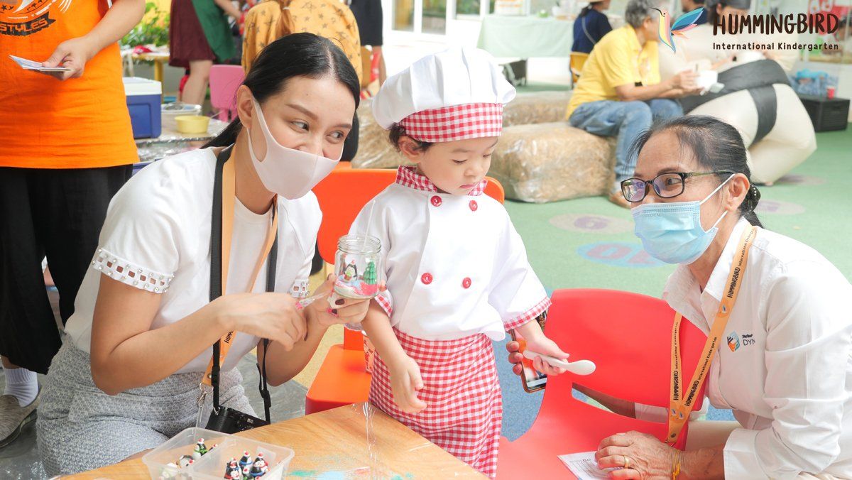 A little girl in a chef costume is sitting at a table with a woman wearing a mask.