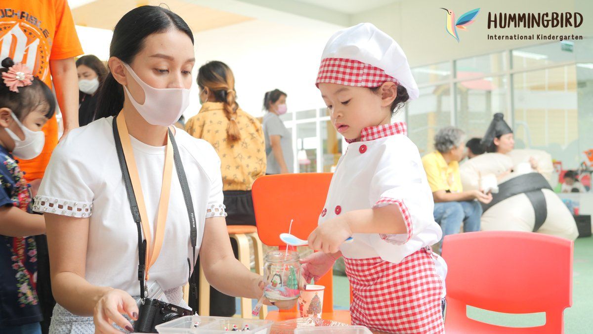 A woman wearing a mask is standing next to a little girl in a chef costume.