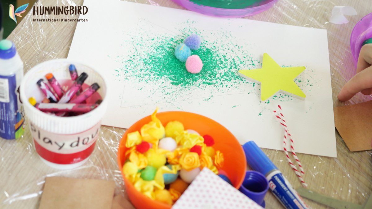 A table with a bucket of crayons and a bowl of pom poms