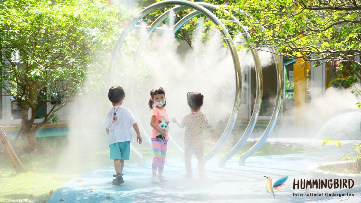 Three children are playing in a sprinkler in a park.