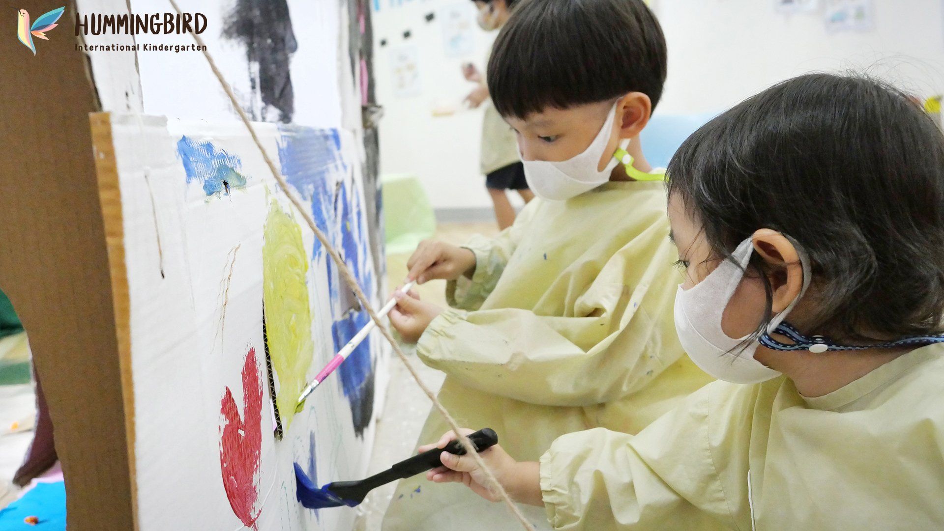 A boy and a girl wearing masks are painting on a wall.