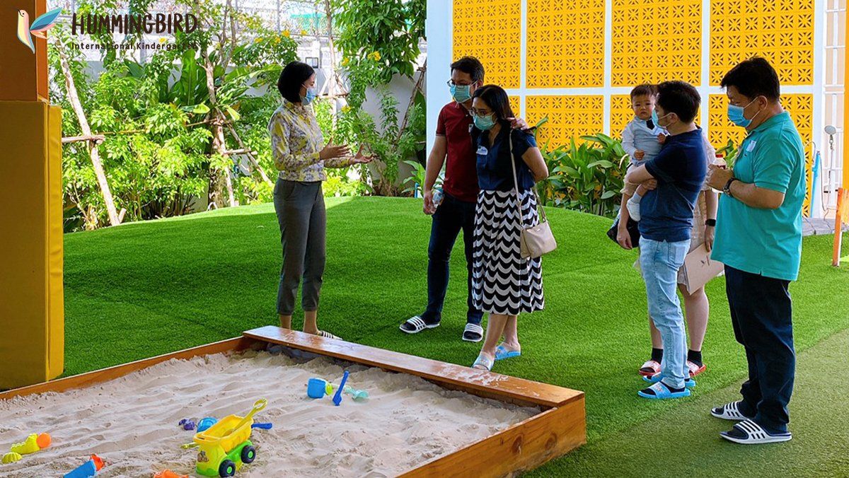 A group of people wearing masks are standing around a sandbox.