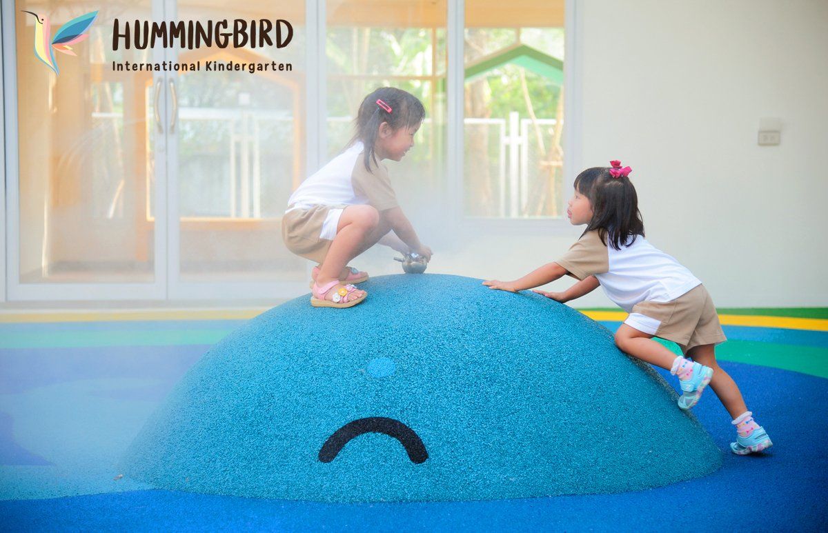 Two little girls are playing on a blue rock with a sad face on it.