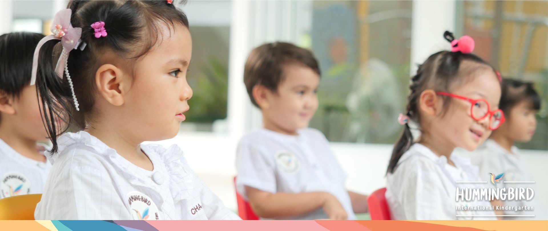 A group of children are sitting in a row in a classroom.