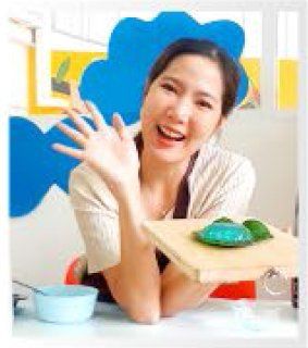 A woman is sitting at a table holding a cutting board with a green object on it.