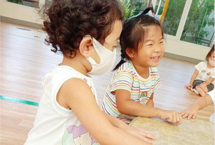 Two little girls wearing masks are sitting on the floor holding hands.