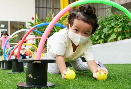 A little girl wearing a mask is playing with balls on the grass.