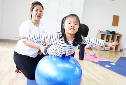 A woman is helping a little girl balance on a blue exercise ball.