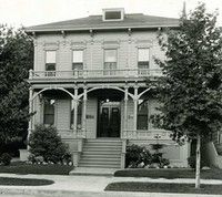a black and white photo of a large house with a porch surrounded by trees . Second location of W.F Gormley & Sons Funeral Chapel