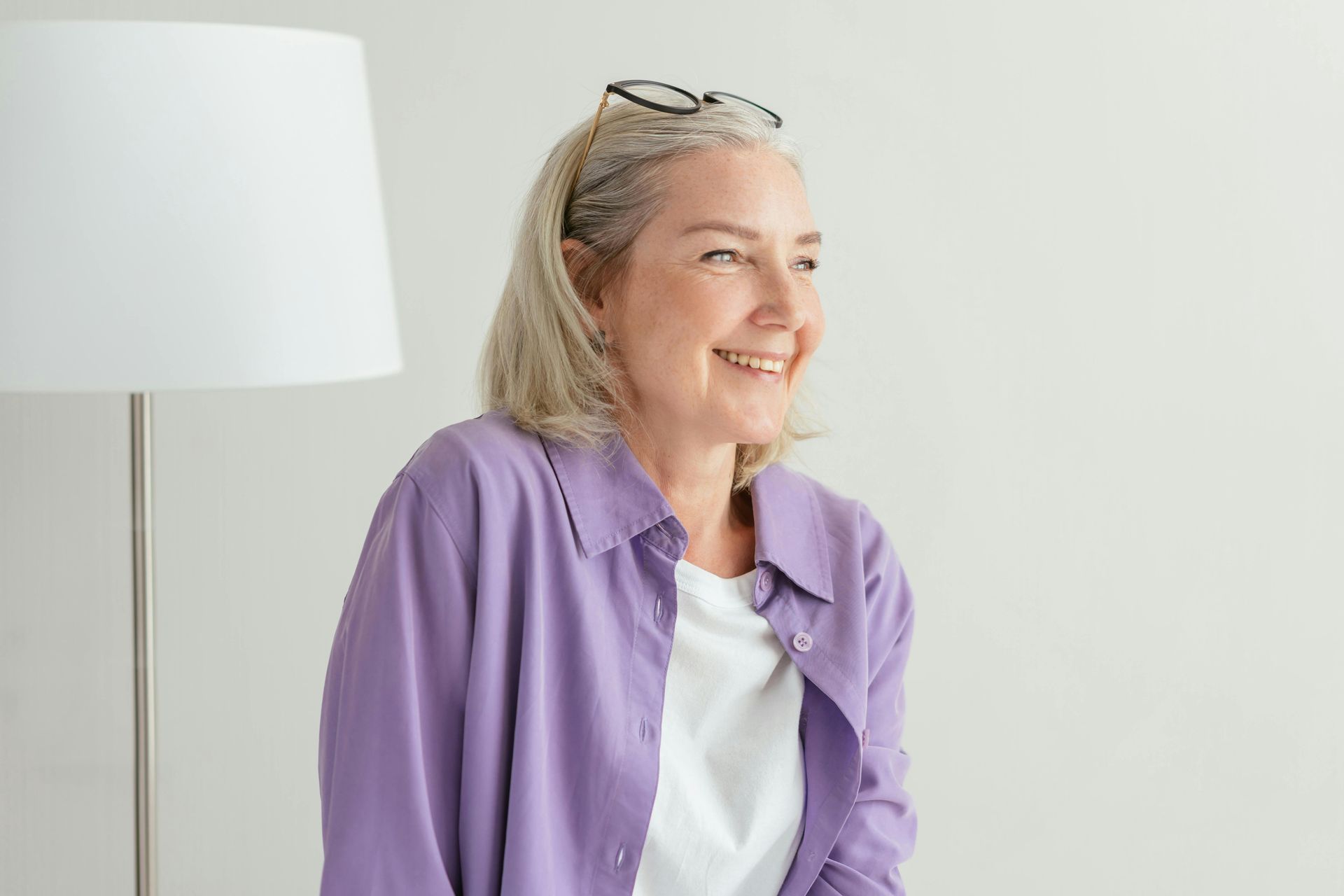 A woman in a purple shirt is smiling while sitting in front of a lamp.