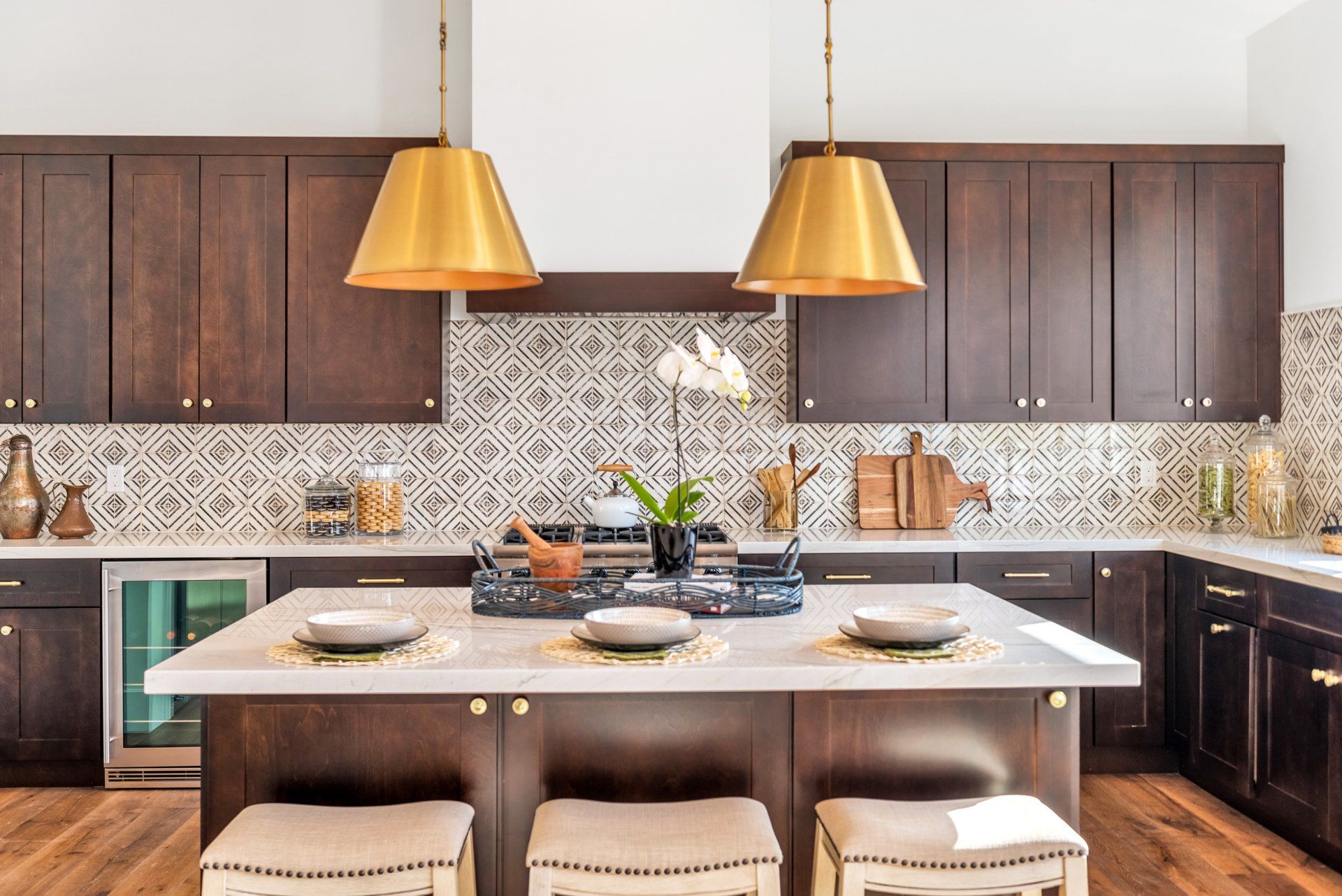 A kitchen with a large island, stools, a stove, and a refrigerator.