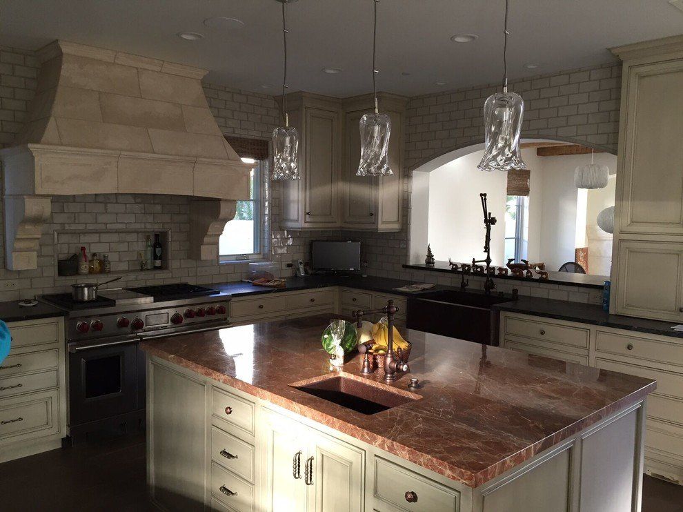 A dimly lit kitchen with a large island that has a sink and white cabinets with black countertops.