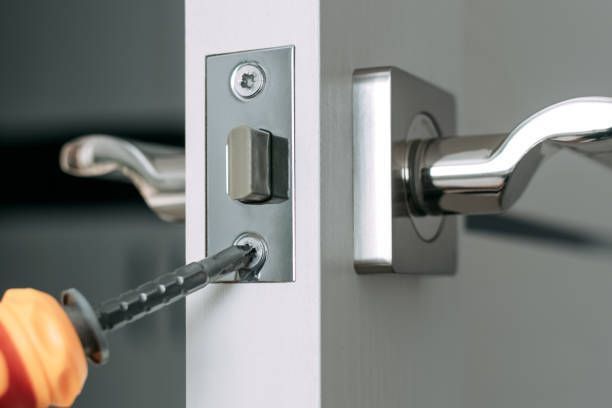 Close-up of a screwdriver adjusting a metal lock on a white door with a silver handle.