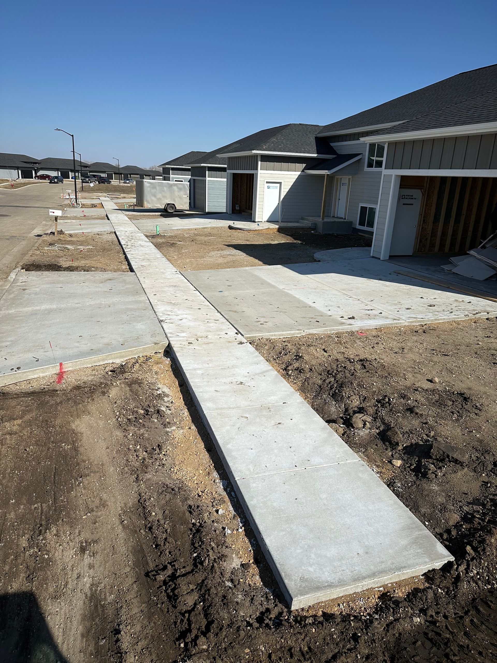 Concrete sidewalk construction in front of new homes with open garage doors; sunny day.