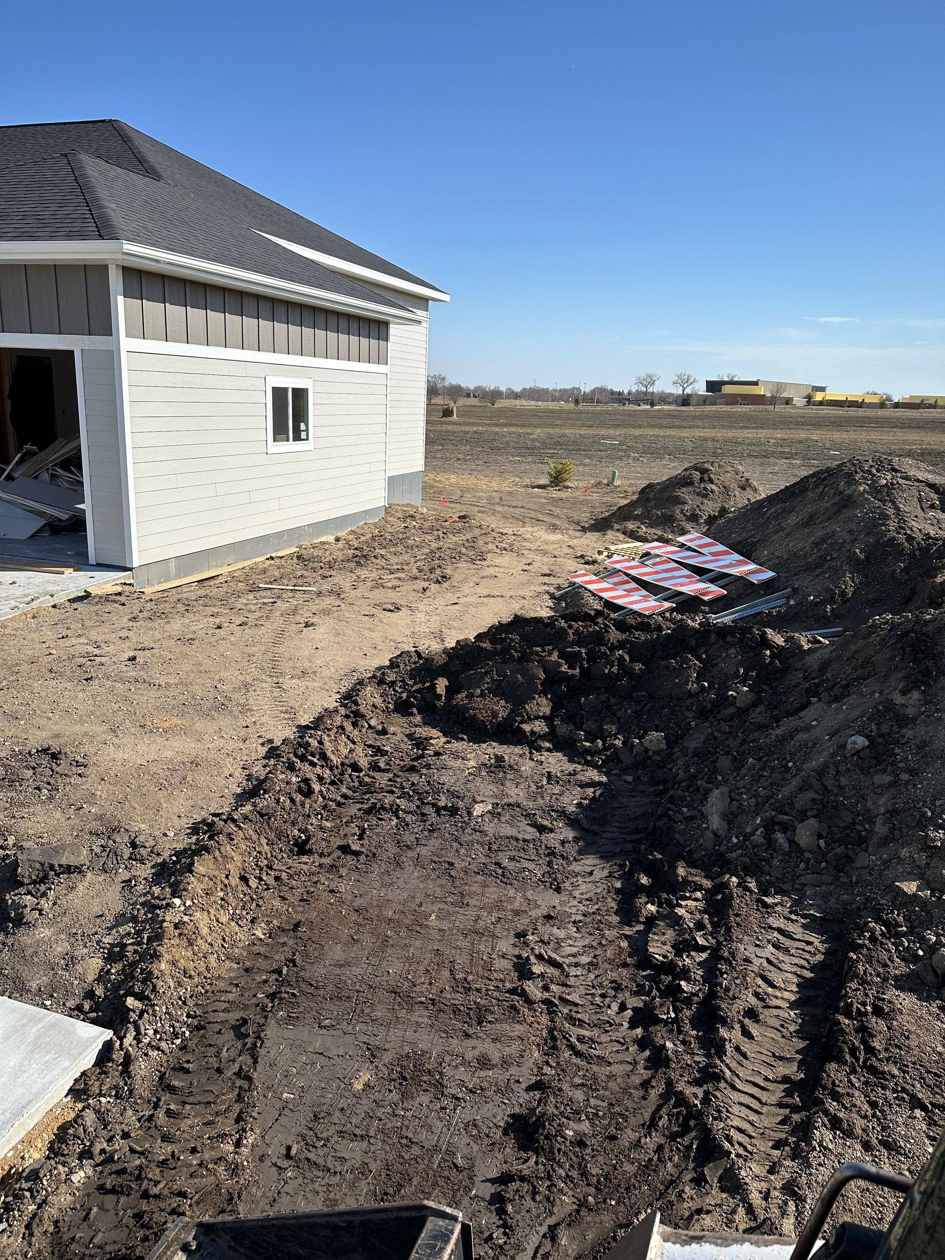 Construction site: House next to a dirt pit with pink insulation visible. Clear, sunny sky.