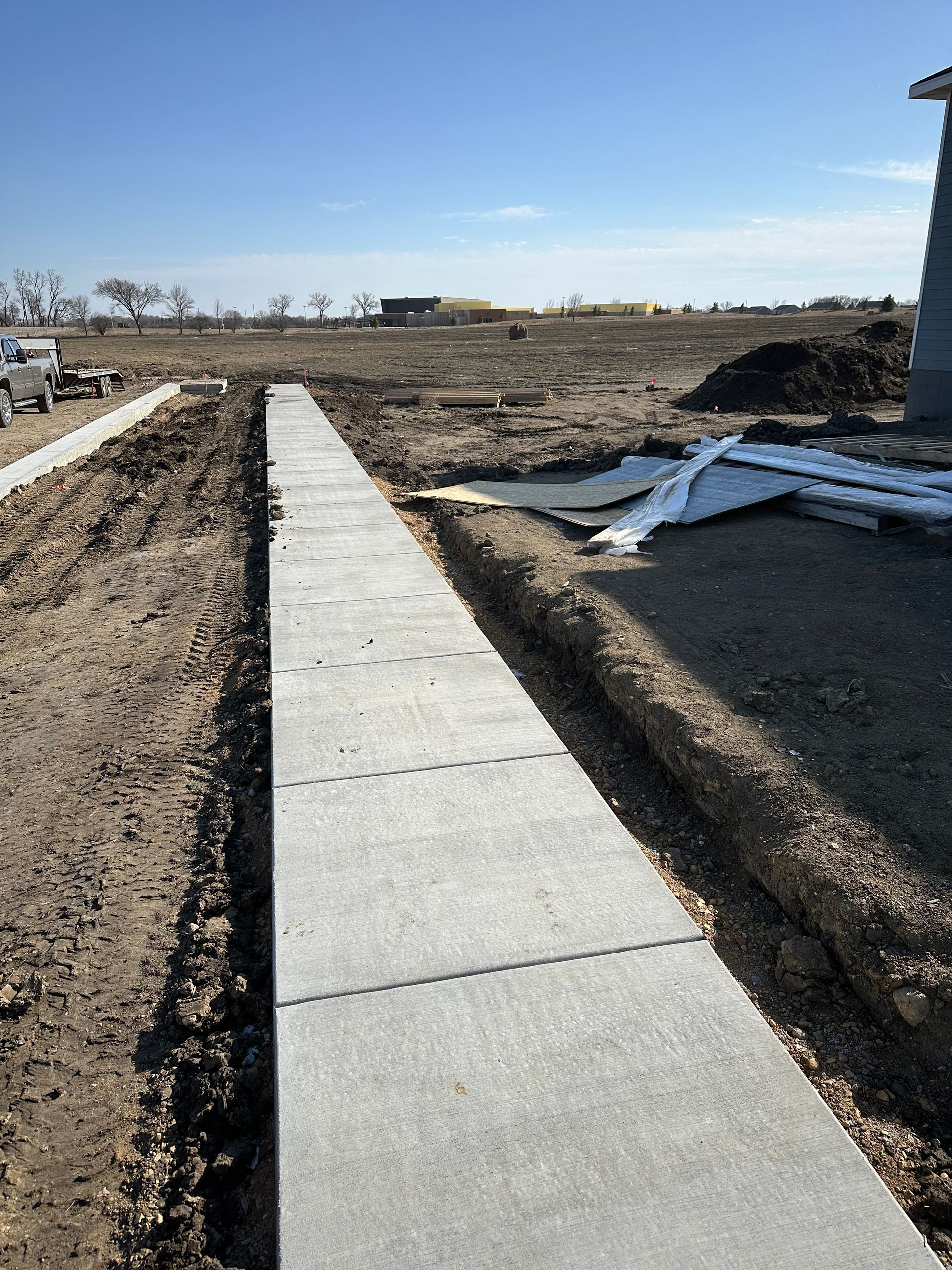 Newly constructed concrete sidewalk in a dirt lot under a blue sky.