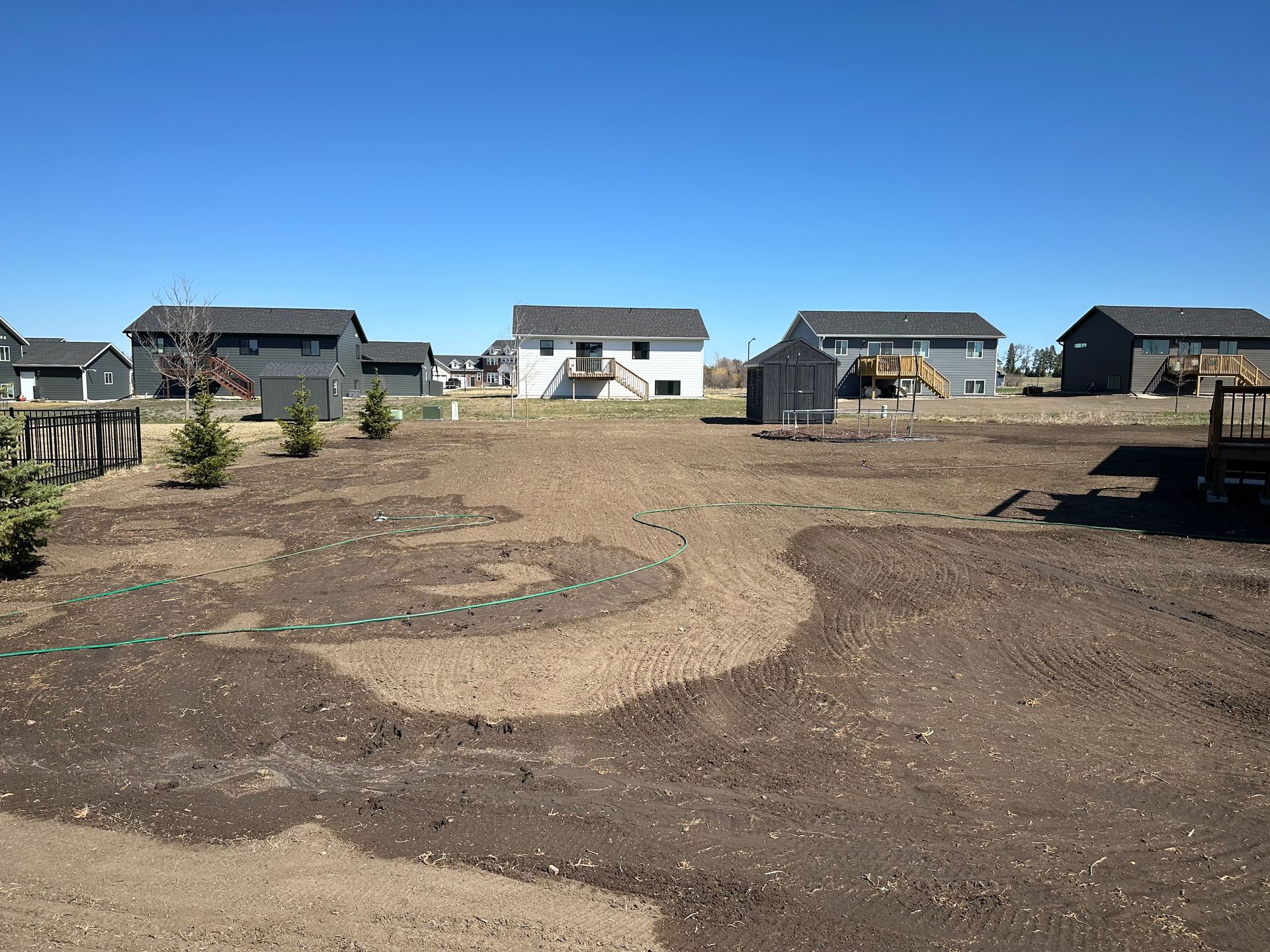 A backyard with newly tilled soil in a decorative pattern, houses in the background under a blue sky.