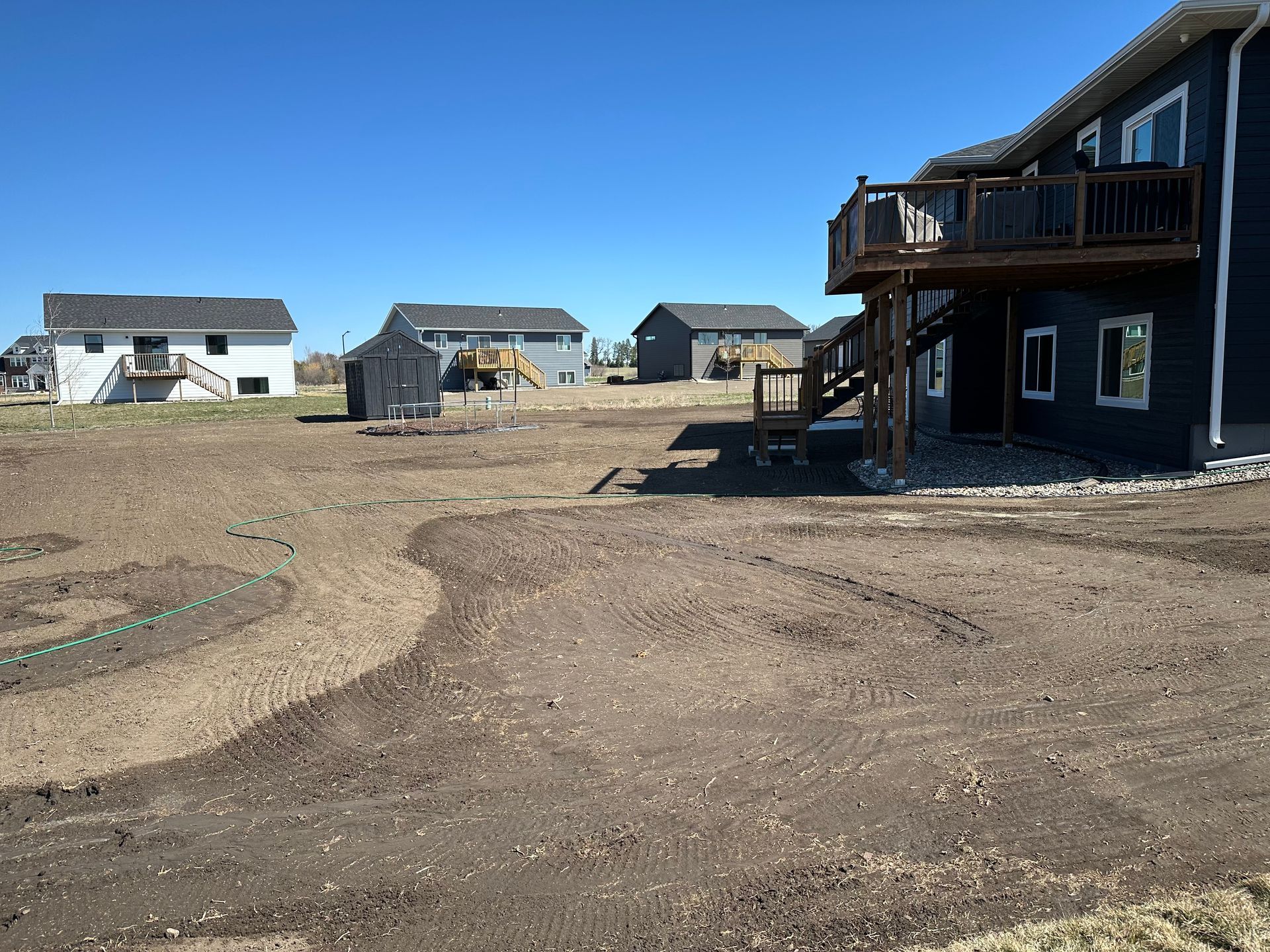 A newly constructed house with a partially landscaped yard and adjacent houses under a clear blue sky.