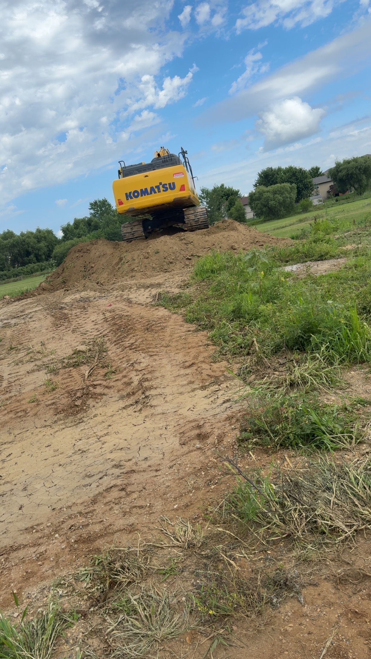 Yellow Komatsu excavator on a dirt mound under a blue sky, performing earthwork.