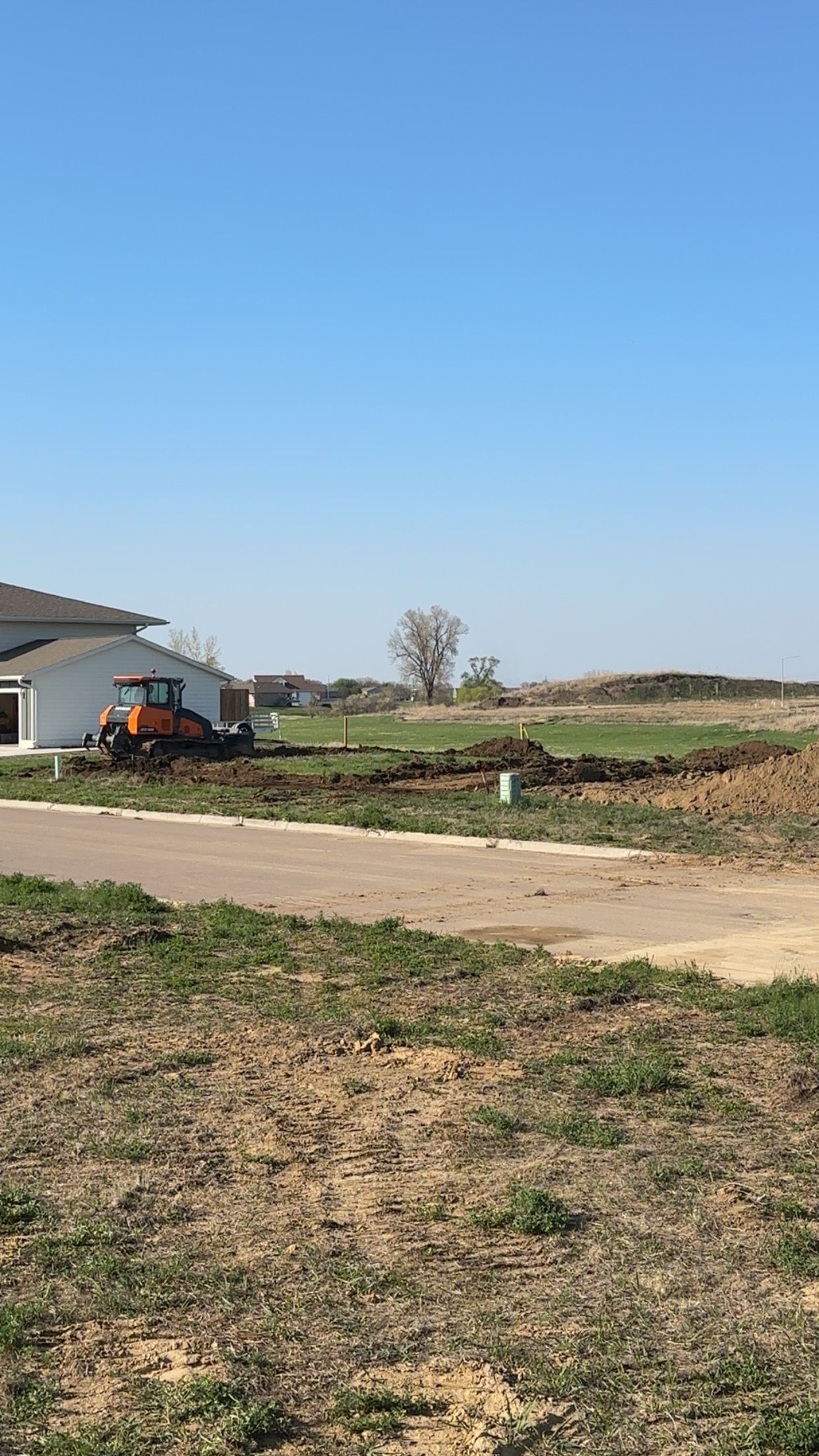 Construction site with bulldozer, house, and dirt mounds under a clear blue sky.