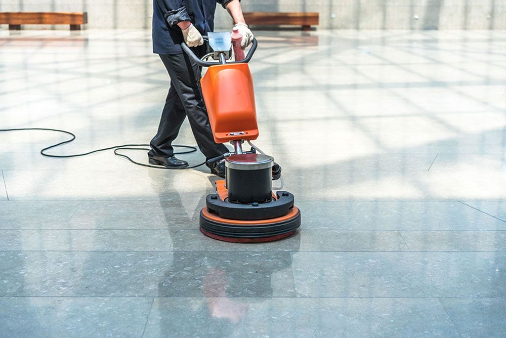 Person using a floor polishing machine on a large, reflective floor in a modern building.