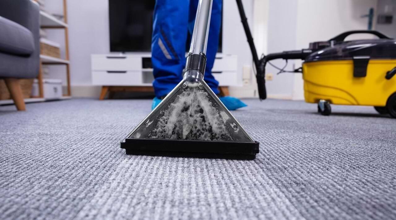 Person in blue cleaning carpet with a vacuum, focused on the cleaner head.